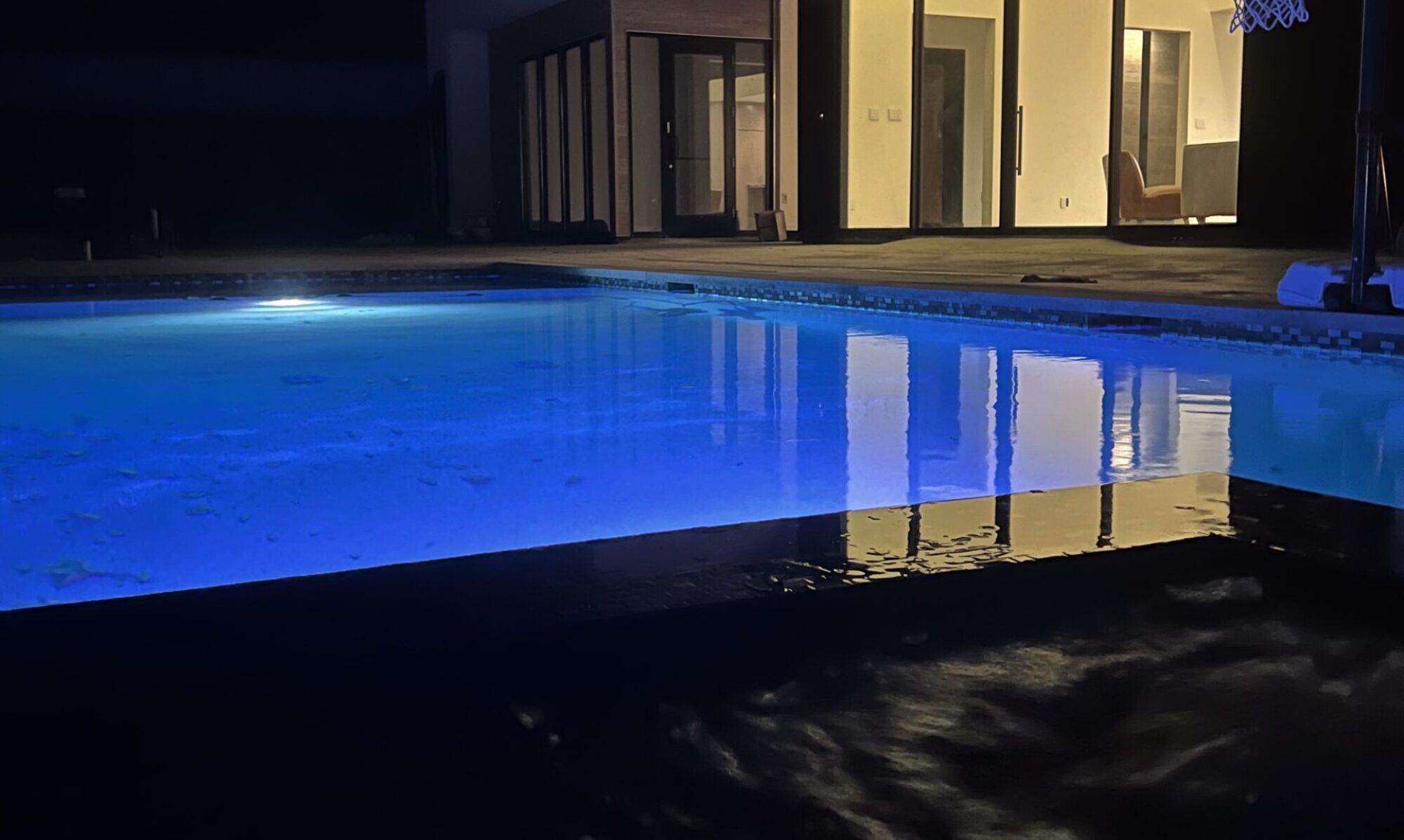 image showing lighted custom pool outside home at night.